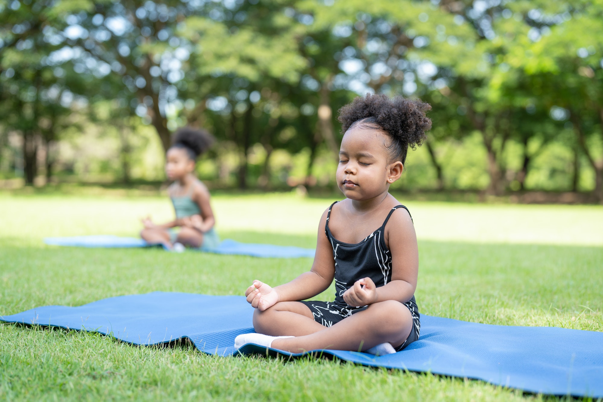African american little girls their eyes closed sitting on roll mat practice meditation yoga in park